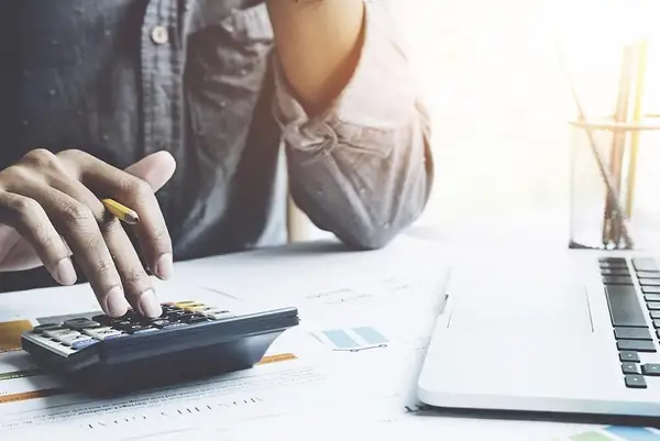 Hands using a calculator next to a laptop